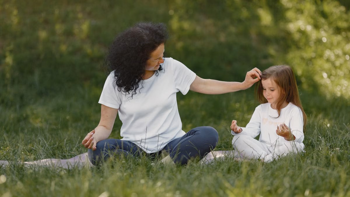 Mother and daughter bonding through yoga outdoors in a serene grassy field.